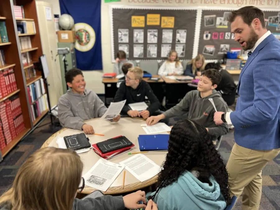 teacher in blue blazer and students speaking in a circle at a table